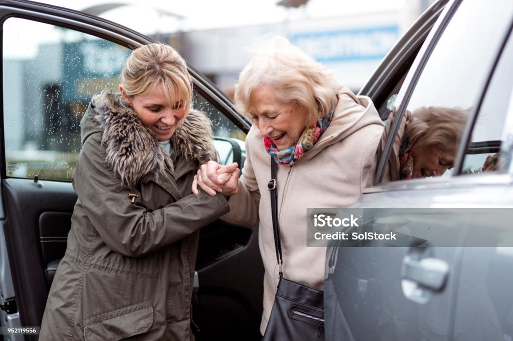 A mature woman helps a senior woman out of a car as she takes her to the shops